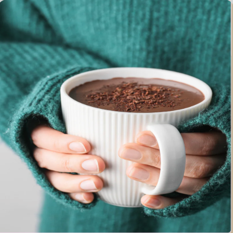 Person holding a white mug of hot chocolate with a green sweater